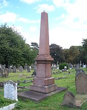 Une grande obélisque rouge à quatre côtés entourée de pierres tombales beaucoup plus petites.