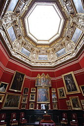 Vue en contre-plongée de la salle octogonale décorée de tentures rouges et de tableaux et surplombée d'une verrière
