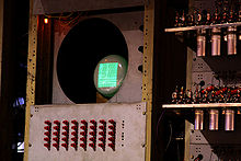 Un petit écran cathodique dans un cadre jaune-marron rouillé qui montre un écran rectangulaire vert sur lequel sont affichés des traits et des points. Dessous, il y a une série de 40 interrupteurs rouges disposés en 8 colonnes de 5.