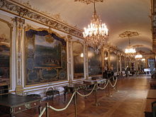 Vue d'une salle tout en longueur couverte de grandes toiles et comportant plusieurs meubles le long d'un des longs murs