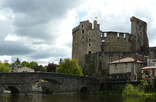 Photographie du château de Clisson prise en avril 2009 depuis la rive sud est opposée ; les hautes ruines se détachent sur fond de ciel nuageux ; au premier plan coule la Sèvre nantaise enjambée par un pont de pierre.