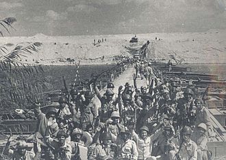 Photographie montrant au premier plan des soldats égyptiens posant devant un des ponts construits sur le canal de Suez