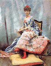 Portrait de Laure Hayman, assise de trois quarts sur un fauteuil, les deux mains reposant sur accoudoir de droite et les pieds gainés de bas rouges et chaussés de même couleur reposent sur un gros coussin bicolore, jaune paille au-dessus, rouge en-dessous.  Le bleu, le rose et le rouge dominent dans cette œuvre, donnant une impression de légèreté, de jeunesse, de luminosité. Le rouge se retrouve dans le nœud qui surmonte des cheveux bouclés serrés en chignon, dans celui qui enserre le cou, dans celui qui orne la pointe du décolleté bordé d’un volant de la robe bleue et jaune dont les manches arrêtées à hauteur des coudes se terminent elles aussi par un volant, et dont la jupe, ouverte sur le devant, s’achève en traine. Du rouge encore pour la jupe de fond recouverte de cinq volants de tulle ou de mousseline qui donnent par transparence un effet rose incarnat rappelant celui des lèvres et des joues fardées. Un bleu et un rose plus légers forment aussi la trame de la draperie en arrière fond.