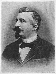 Léon Tailhade  avec bouc et moustache, vêtu d'une veste, avec un nœud papillon sur une chemise à col droit.