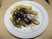 Dans une assiette blanche, quenelles de pommes de terre nappées de sucre fondant et de graines de pavot.