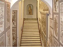 Perspective dans le département des mosaïques romaines vu de l’escalier d’accès avec des mosaïques au mur et une statue d’Apollon au fond.