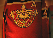 Un maillot rouge avec des bandes noires. Une feuille d'érable et les mots Edmonton Mercurys et 52 Olympics y figurent.