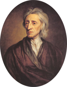 Portrait de trois-quarts d'un homme aux cheveux blancs portant une large veste brune et une chemise blanche.