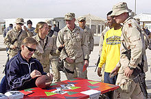 Photographie de John Elway lors qui signe un autographe sur un ballon entouré de militaires américains