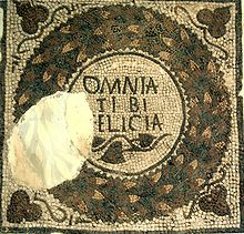Pavement montrant la phrase « Omnia tibi felicia » au milieu d’une guirlande de feuilles.