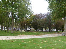 Photographie du jardin public montrant des allées sablées ponctuées de bancs, délimitant des pelouses plantées de hauts platanes ou d'essences d'arbres variées.
