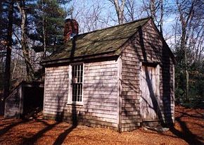La cabane de pin de Thoreau à Walden, reconstituée. Il s'agit d'une petite maisonnette au toit gris et aux murs de bois, entourée d'arbres.